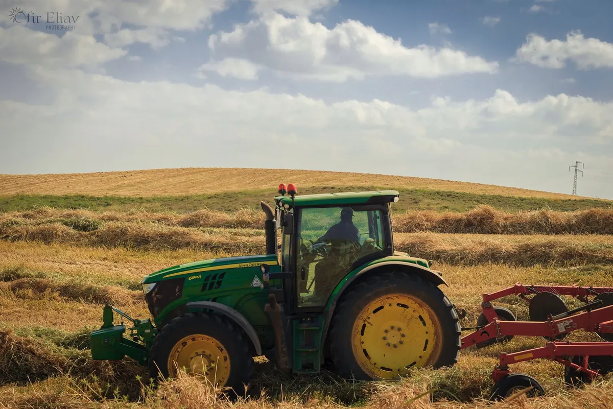 Tractor pulling an implement across a paddock at harvest time