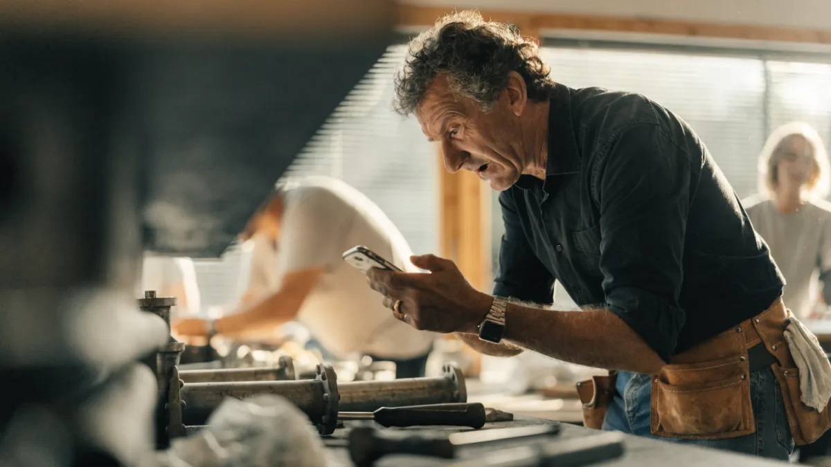 Tradesperson using a smartphone in a busy workshop