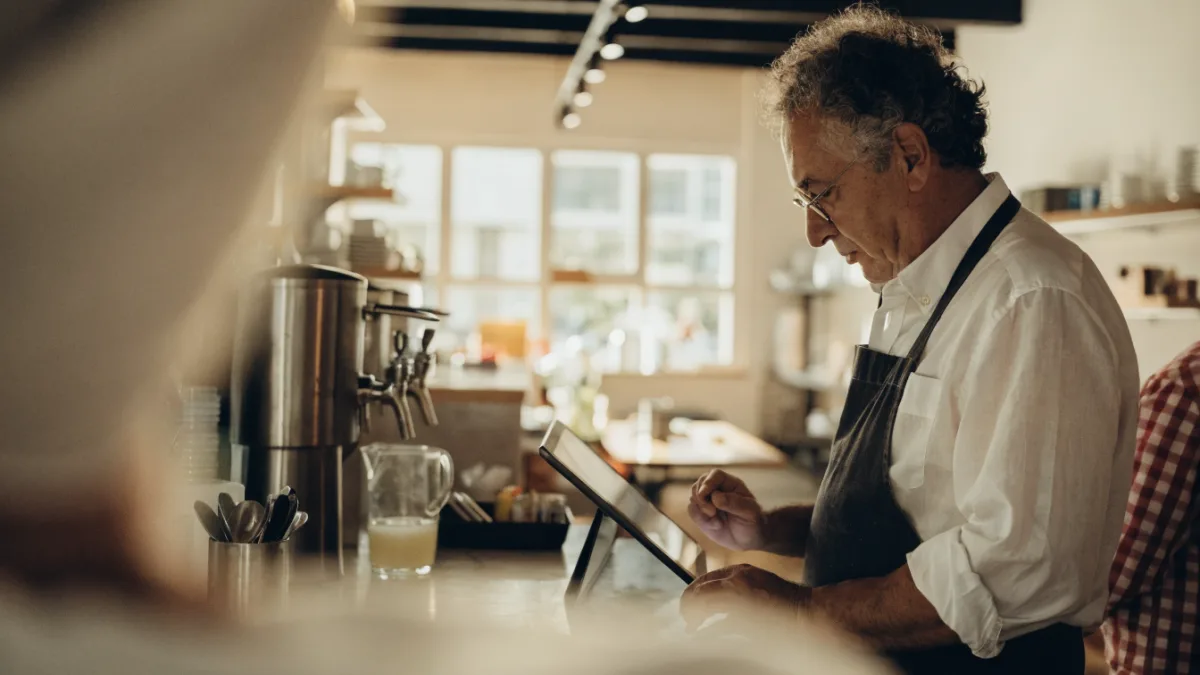 Cafe owner checking cash flow on a tablet at the counter
