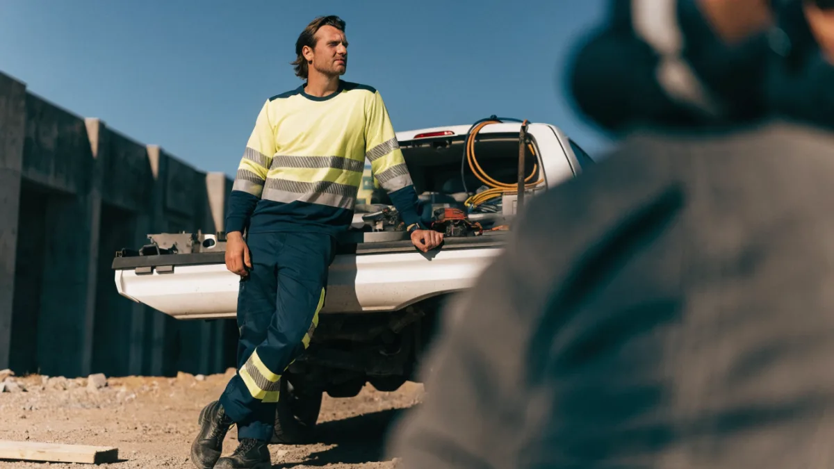 Tradie in hi-vis beside a work ute loaded with tools on a job site