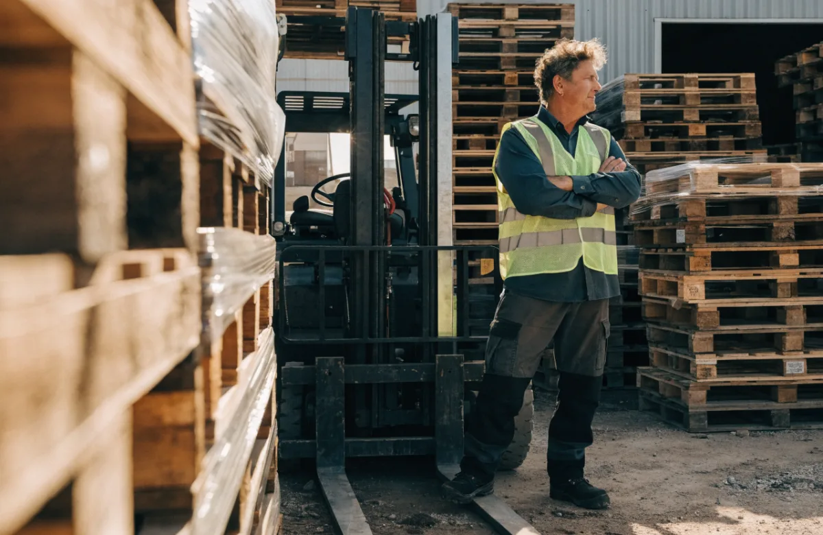 Business owner in hi-vis beside a forklift in a warehouse
