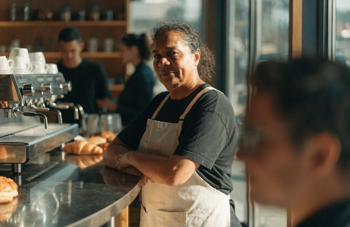 Café owner in an apron standing behind the counter of a busy café