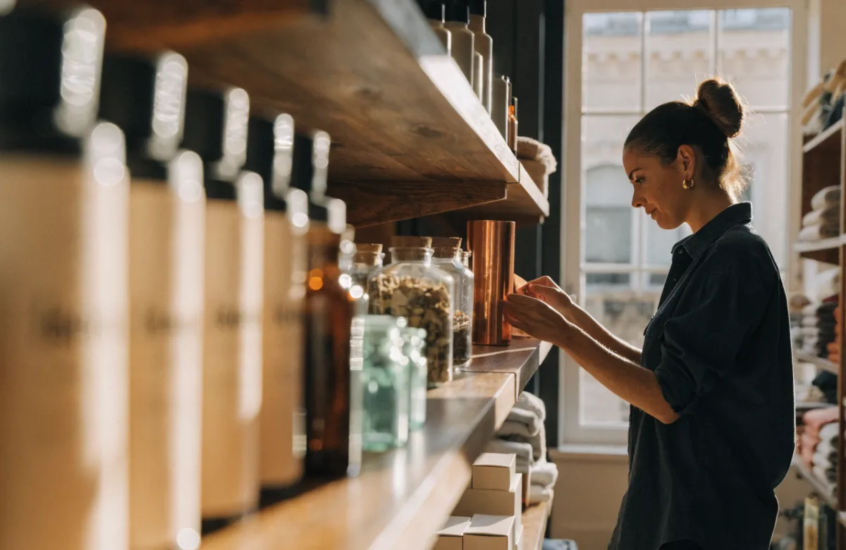 Retail store owner arranging products on shelves in a bright shopfront
