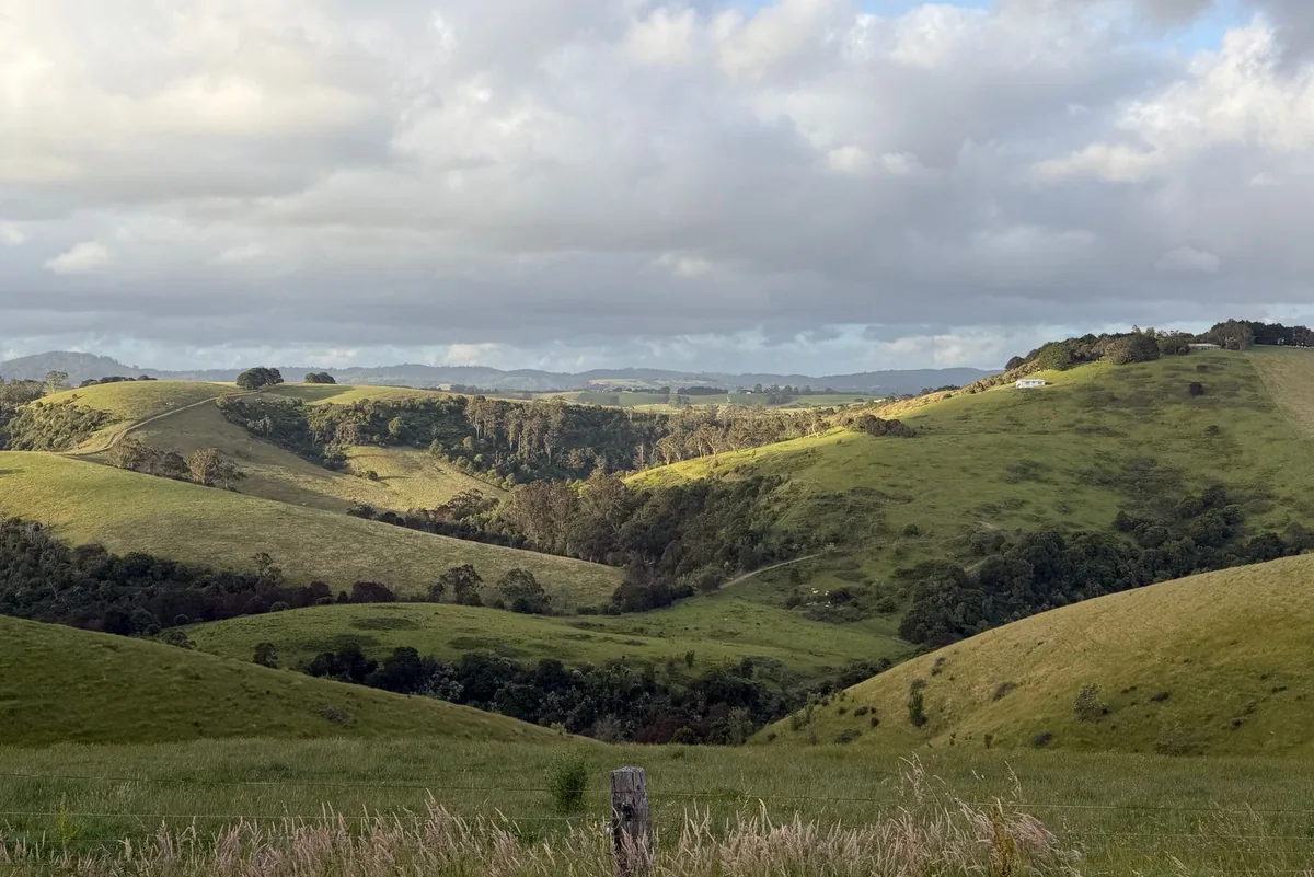 Rolling green farmland and wooded hills under a cloudy sky